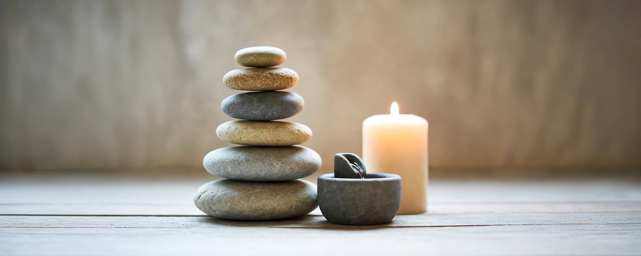 A stack of smooth river stones beside a small stone fountain and a lit candle